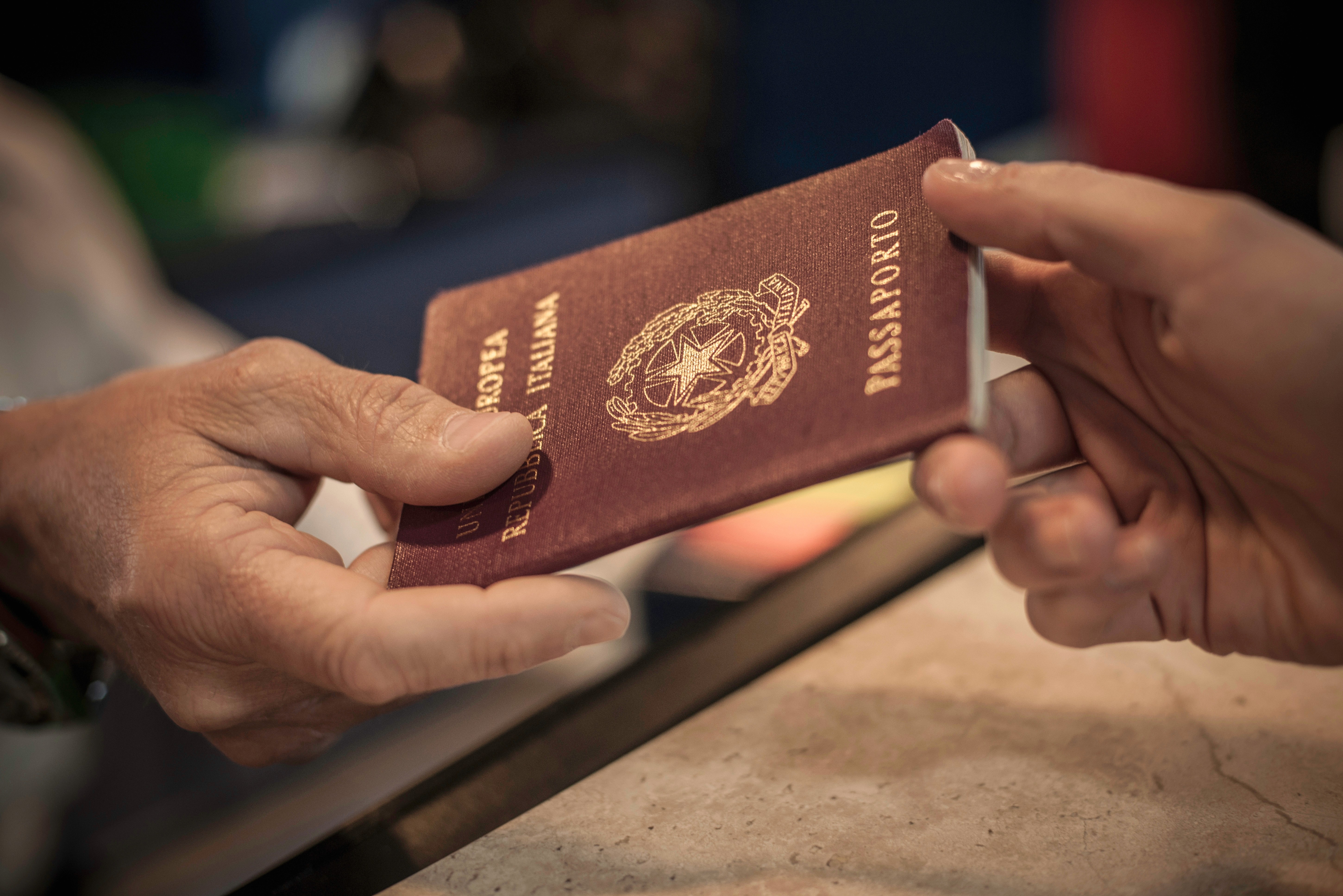 Na imagem, uma pessoa entrega um passaporte italiano para outra, com foco nas mãos e no documento