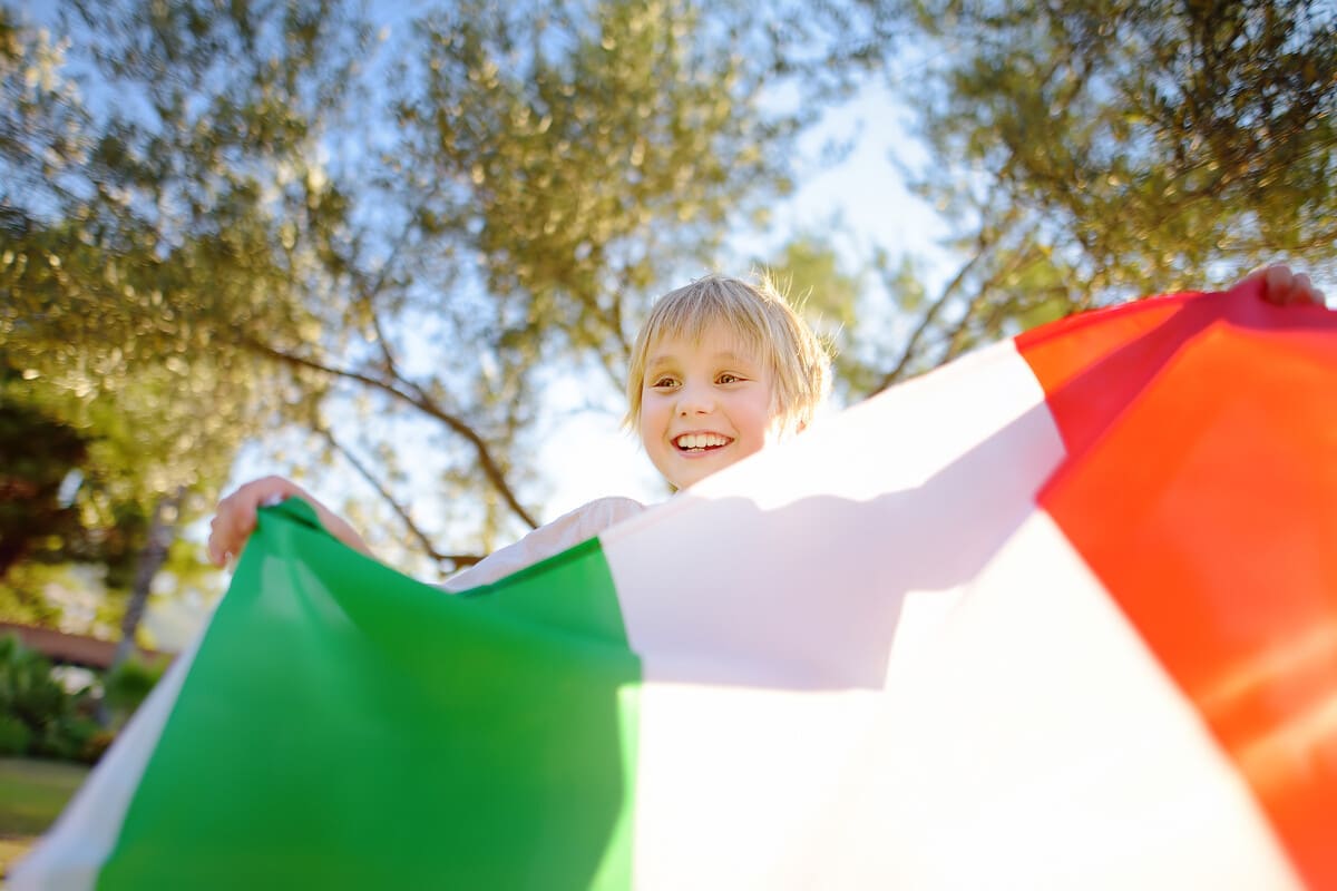 Menino loiro balançando a bandeira da Itália. O que representa o Dia da Unidade Nacional, da Constituição, do Hino e da Bandeira na Itália