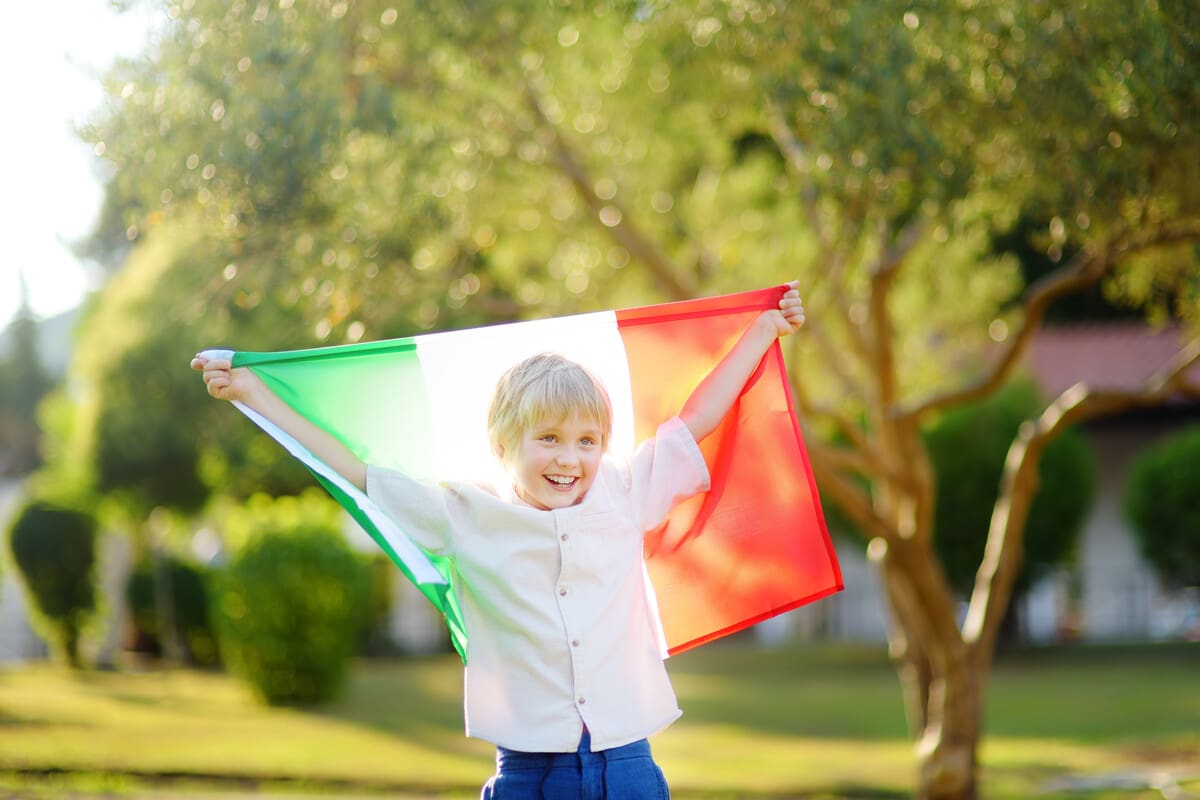 Menino branco e loiro segurando a bandeira da Itália. 7 motivos para tirar sua cidadania italiana e expandir suas oportunidades na Europa