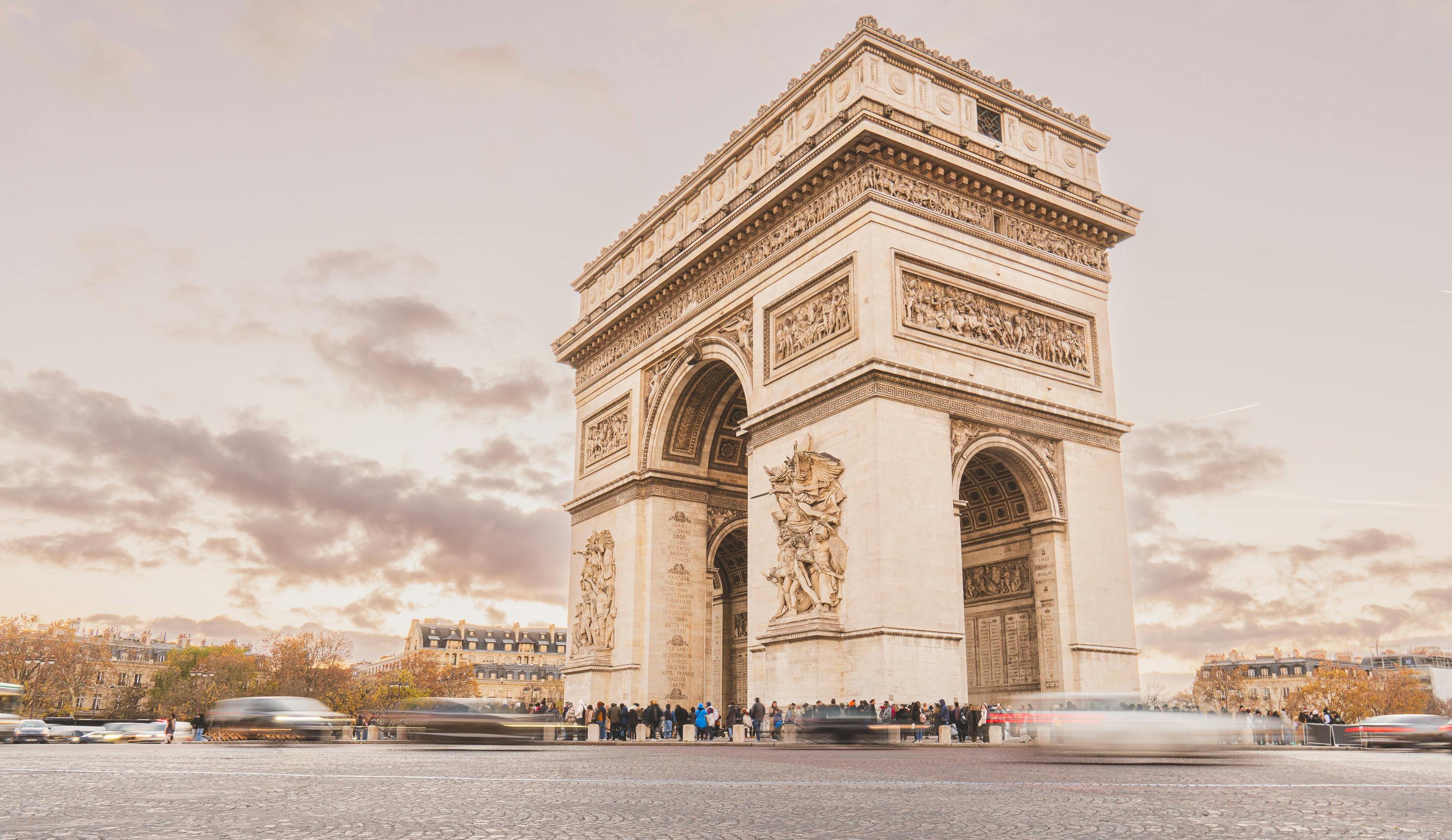 Imagem do arco do triunfo, com transeuntes representados como um borrão para expressar movimento, e algumas nuvens ao fundo