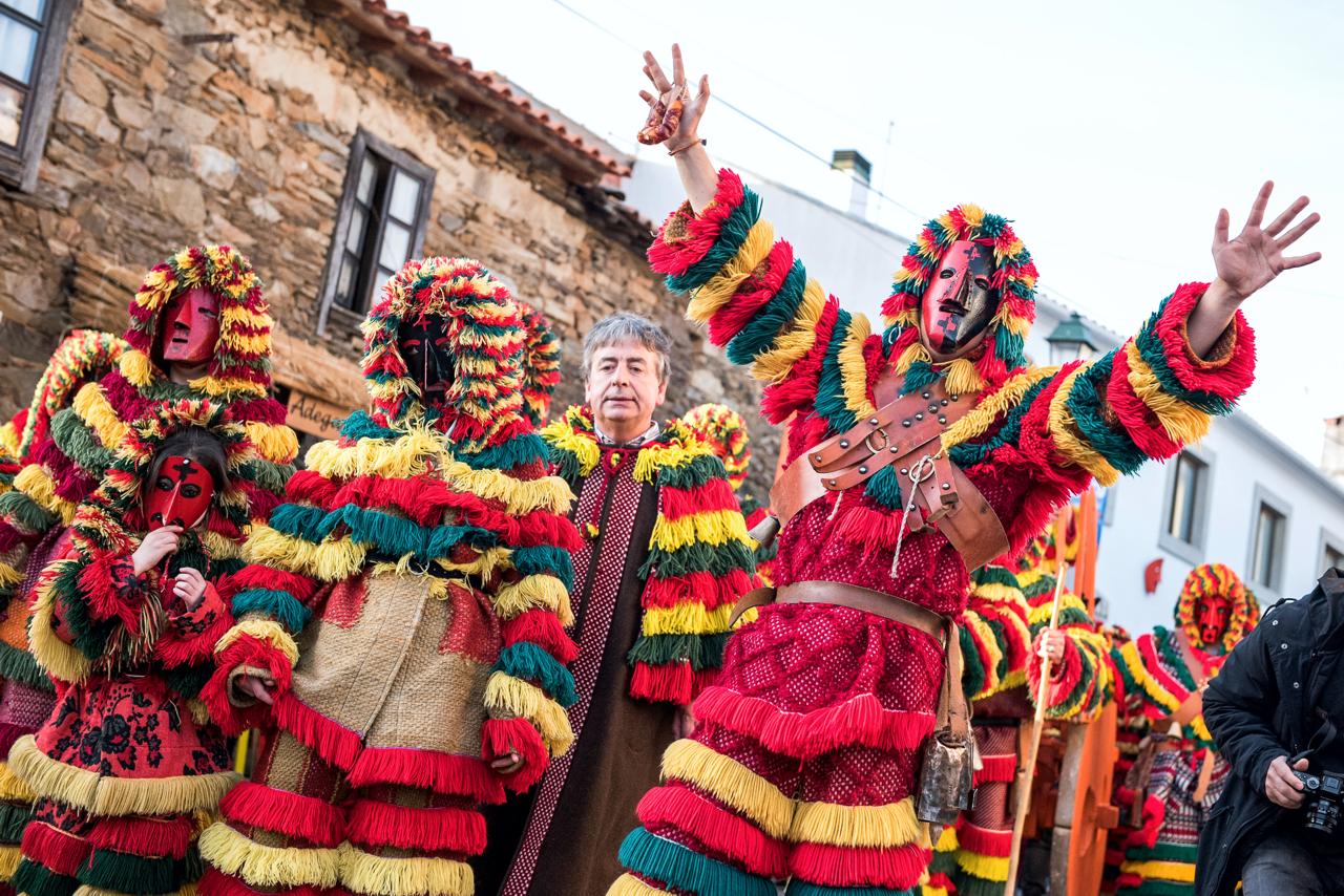 Homens fantasiados de Caretos, trajando vestes vermelhas, com algumas listras amarelas e verdes, em franjas e com capuz. Também carregam uma máscara ao rosto.