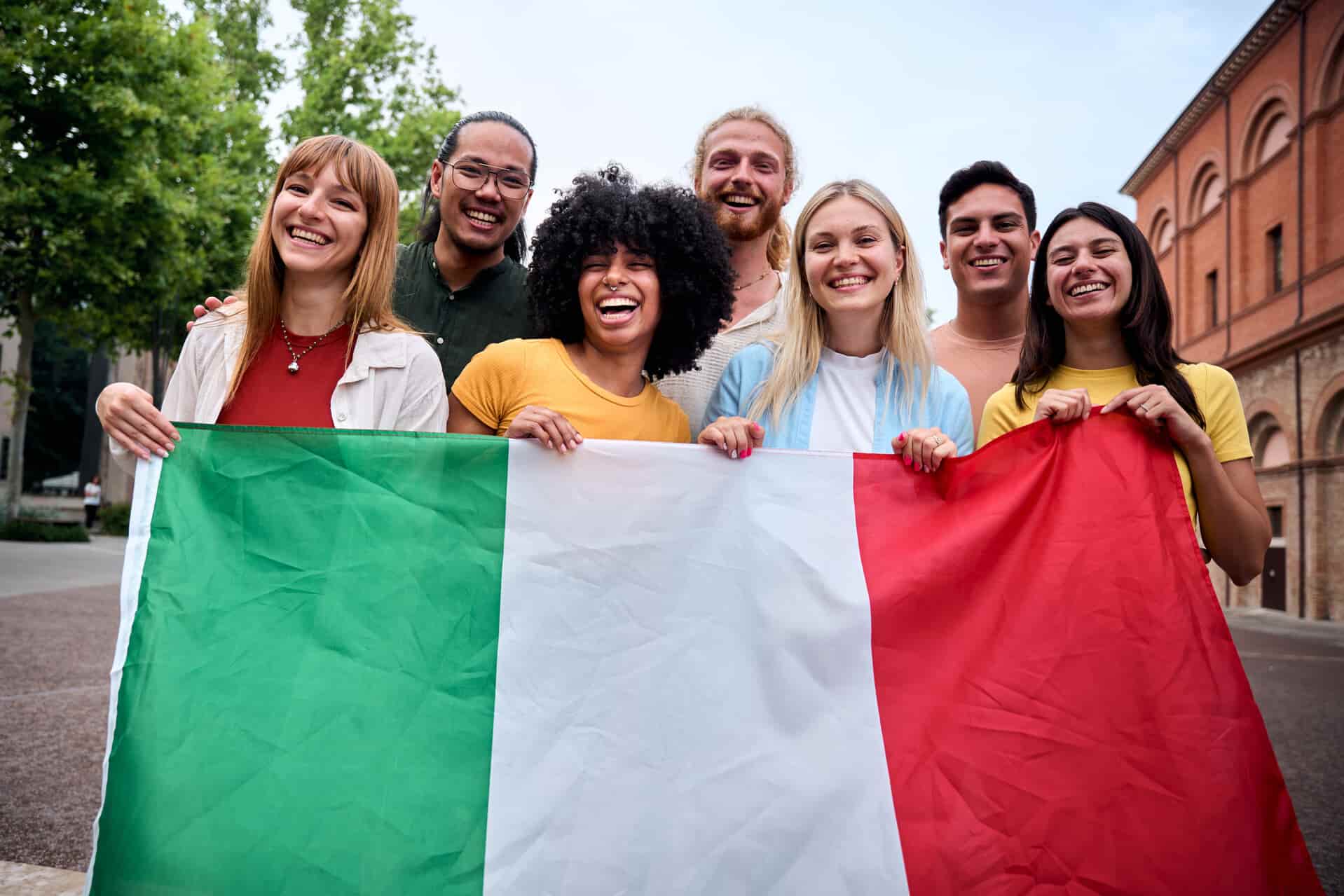 Grupo multiétnico de jovens segurando a bandeira da Itália. 7 motivos para tirar sua cidadania italiana e expandir suas oportunidades na Europa