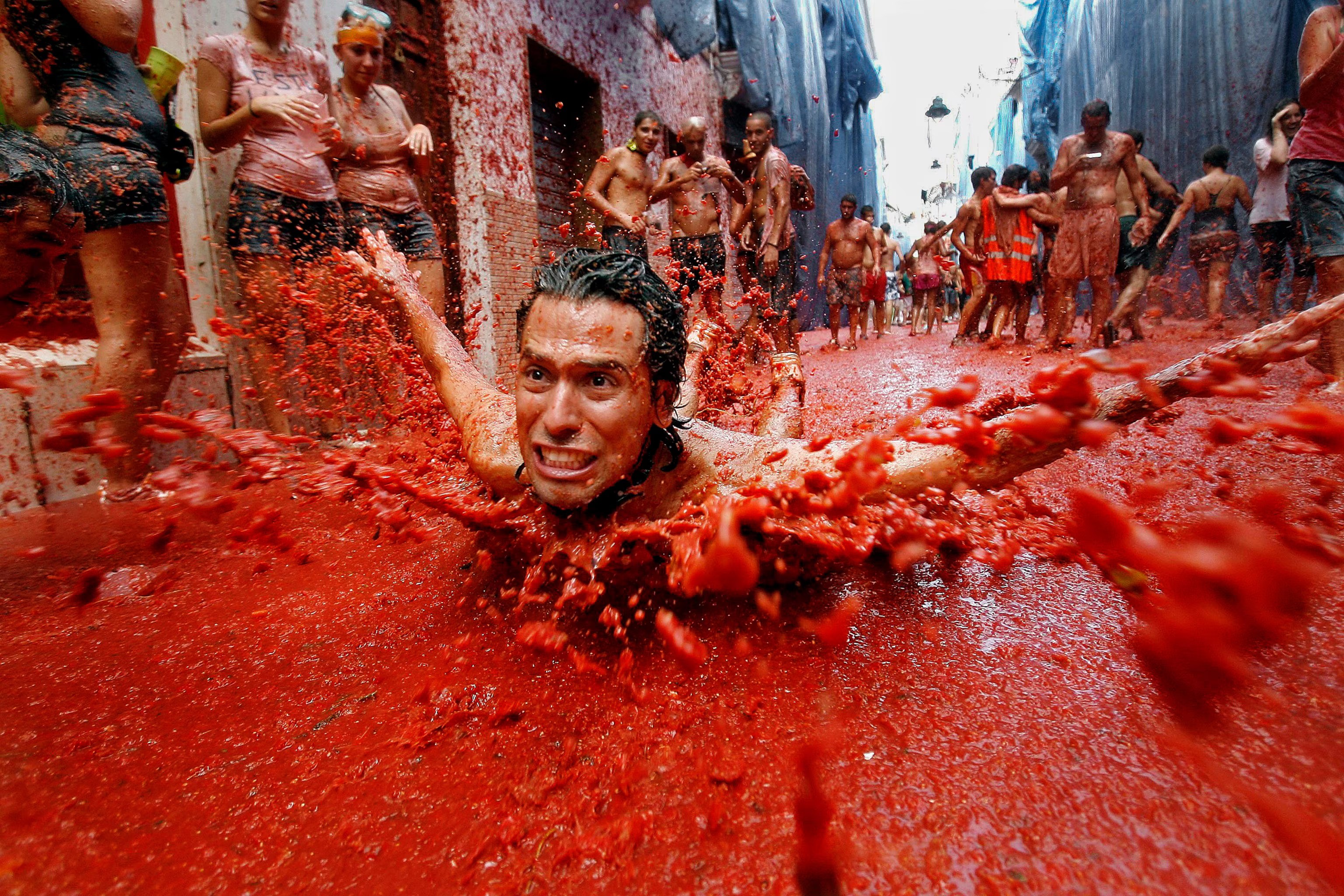 Homem sem camisa deslizando de barriga em polpa de tomate, que cobre uma das ruas de Buñol, na Espanha, cidadezinha onde acontece anualmente a La Tomatina.