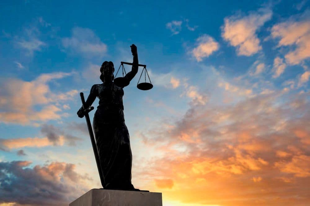 Imagem da estátua da justiça, com um céu azul e alaranjado ao fundo e o sol se pondo.