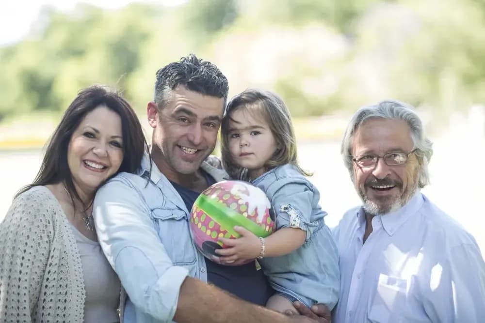 Família de quatro pessoas posando com um cenário verde ao fundo. Da esquerda para a direita: uma mulher de cabelos escuros, um homem com cabelo acinze