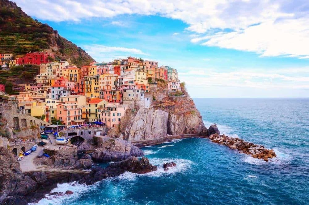 Visto de Cinque Terre, com as casas coloridas, o céu azul com algumas nuvens e o mar.
