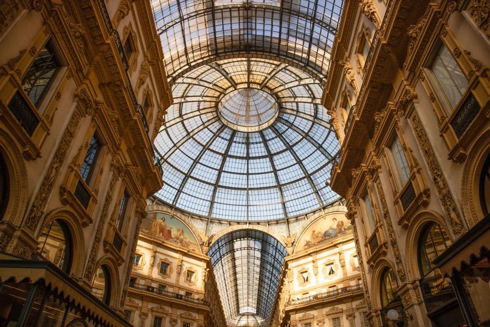 Vista da Galeria Vittorio Emanuele II por dentro, com foco na abóbada central que coroa a grande cobertura de vidro do lugar.