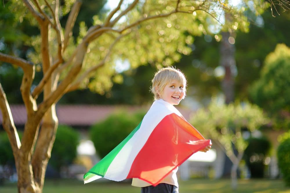 Criança de cabelos loiros segurando a bandeira italiana