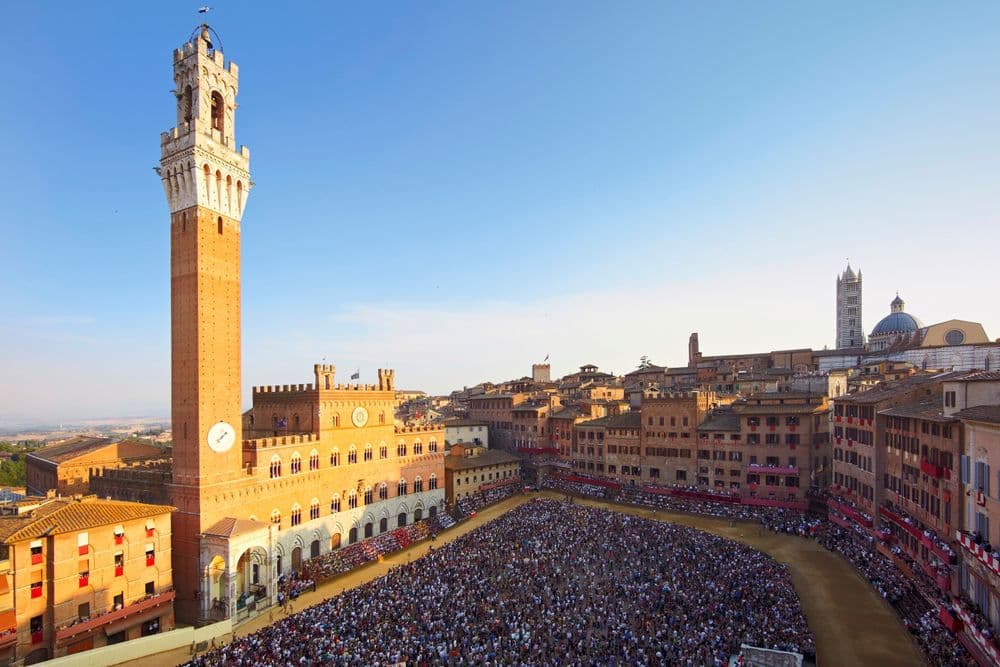 Vista ampla da Piazza del Campo, em Siena. Principal ponto da cidade, é onde ocorre o Palio di Siena todos os anos. Várias pessoas, uma multidão se re