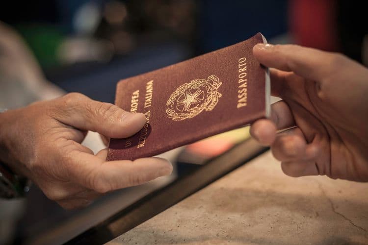 Na imagem, uma pessoa entrega um passaporte italiano para outra, com foco nas mãos e no documento