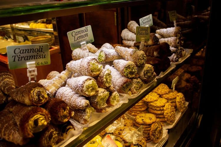 Diferentes tipos de Cannoli, como Cannoli de Tiramisù e Cannoli de Limão, em exibição no balcão de uma confeitaria.